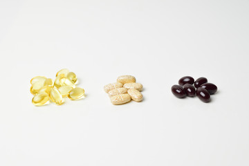 Three bunches of multivitamins, fish oil and astaxanthin. Vitamins in the middle. White background. Close-up.