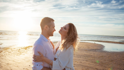 Love, romance, walk. Airy portrait of beautiful couple kissing on background of sunset sea, sandy beach and clouds.