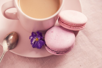 Two pink macaroons on the plate near cup with coffee