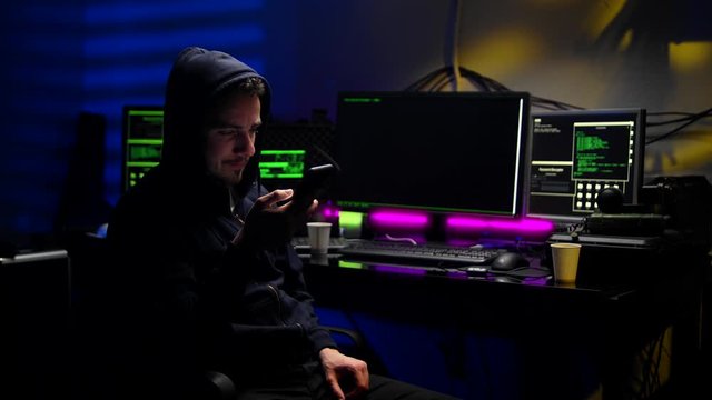 A young man in a hood with a phone in his hands. Hacker makes a hack through the phone.