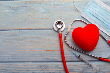 Red heart, face mask, stethoscope and syringe on wooden background. Health concept.