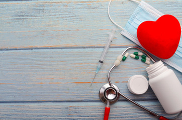 Red heart, face mask, stethoscope and syringe on wooden background. Health concept.