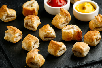 Pork sausage rolls with mustard and ketchup on rustic black stone