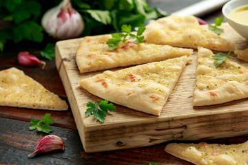 Fresh slices of Garlic pizza on wooden board with herbs.