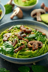 Vegan garlic mushroom pasta with spinach and avocado pesto drizzled with sesame seeds and roasted pine nuts