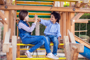 Two smiling kids friends boy and girl sitting on playground outdoor. Childhood and friendship concept