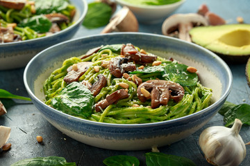 Vegan garlic mushroom pasta with spinach and avocado pesto drizzled with sesame seeds and roasted pine nuts