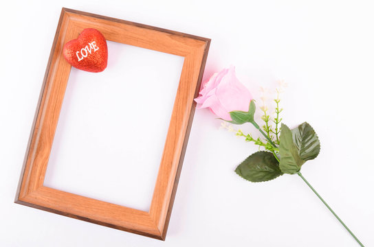 Flat lay view of artificial red roses with heart shape and wooden frame on white background. Love and Valentine's Day concept.