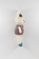 knitted toy rabbit in a sweater-dress with a flower on the ear on a white background