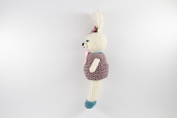 knitted toy rabbit in a sweater-dress with a flower on the ear on a white background