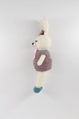 knitted toy rabbit in a sweater-dress with a flower on the ear on a white background