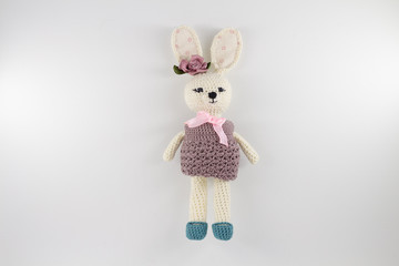 knitted toy rabbit in a sweater-dress with a flower on the ear on a white background