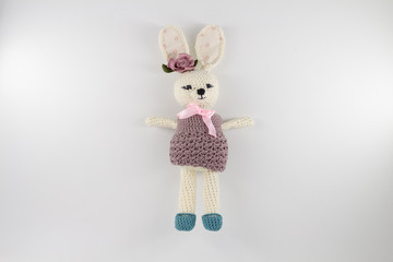 knitted toy rabbit in a sweater-dress with a flower on the ear on a white background
