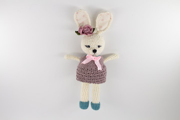 knitted toy rabbit in a sweater-dress with a flower on the ear on a white background