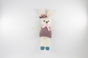 knitted toy rabbit in a sweater-dress with a flower on the ear on a white background