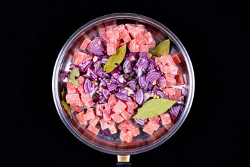Initial ingredients for cooking Goulash.  Pieces of pork, sliced red onion, Bay leaf, allspice. All this is placed in a stainless steel pan.