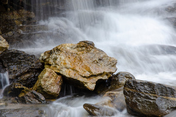 A stone with a flowing waterfall in the background with a blurred patterned background