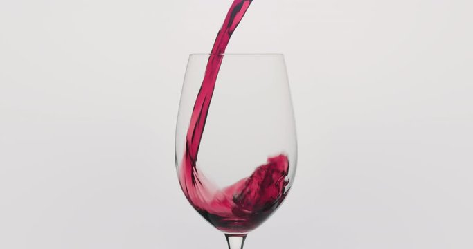 Slow motion red wine pour into wineglass on neutral background