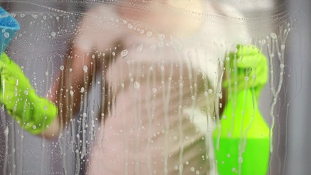 the woman washes a window. Splashes soapy water on the glass. Cleans the glass from dirt.