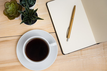 The begining of the work day. Morning at the office. Student workplace. Cup of coffee, notebook with pen and plants on a wooden table. View from above.
