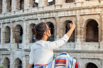 Fototapeta na wymiar Beautiful young woman taking pictures with smartphone sitting in front of colosseum in Rome at sunset.