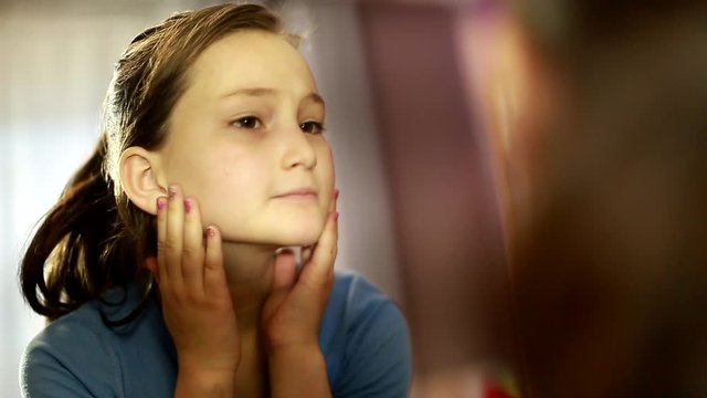 cute girl sitting and looking in the mirror. Teenage complexes. zits. unhappy with her appearance. making faces