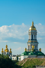 Fototapeta na wymiar Christian church on the green hills. The bell tower with golden domes. Christianity concept. Old church. vertical photo