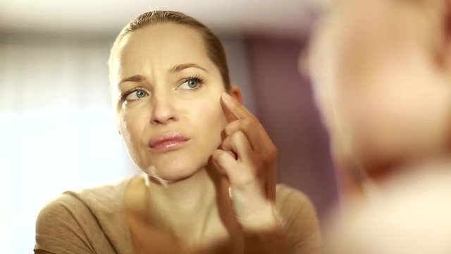 girl looks in the mirror, not pleased with the appearance, pulls the skin. Ugly, aging skin. Allergic to cosmetics, fear of aging, under eye circles, wrinkles. Low self-esteem, dysmorphic disorder. 