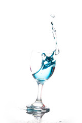Splashing blue water into the crystal wine glass, closely spreading on a white background.