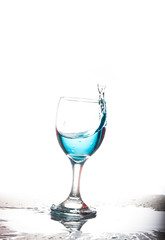 Splashing blue water into the crystal wine glass, closely spreading on a white background.