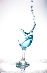 Splashing blue water into the crystal wine glass, closely spreading on a white background.