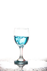 Splashing blue water into the crystal wine glass, closely spreading on a white background.