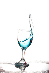 Splashing blue water into the crystal wine glass, closely spreading on a white background.