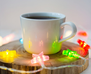 cozy still life with a cup of coffee on a wooden stand and colored garlands of stars