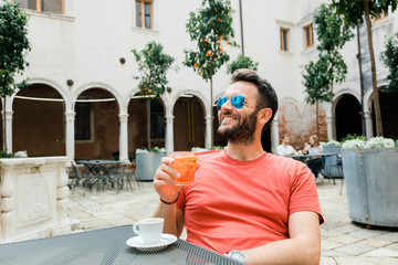 Young handsome man sitting in an outdoor cafe in summer time drinking coffee and cocktail