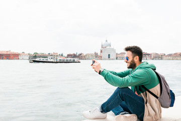 Fototapeta na wymiar Young traveler sitting on the waterfront enjoying the view of canal in Venice, Italy