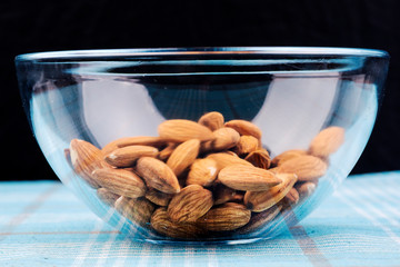 Almonds in a glass bowl isolated on black background.