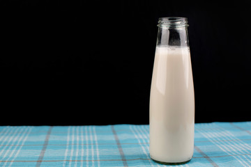 Almond milk in a bottle, on blue tablecloth, on a black background, place for text.