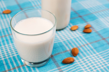 Almond milk in glass with almonds in bowl, on color wooden background