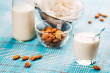 Almond milk in glass with almonds in bowl, on color wooden background