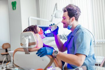 Portrait of a female patient at dentist in the clinic. Teeth whitening procedure with ultraviolet light UV lamp.