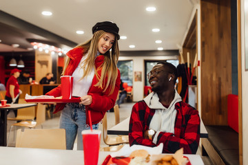 Meeting two happy friends, woman with portion of fast food sit near her best friend.