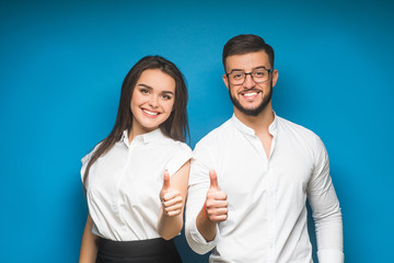 Two confident smiling businesspeople, agent or partners in formalwear showing okay sign on blue background.