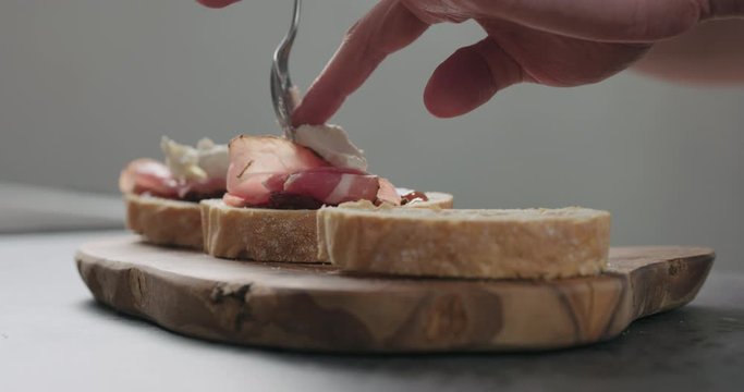 Slow motion man add ricotta to slice of ciabatta with fig marmalade and pancetta
