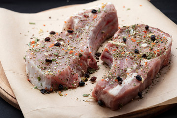 Pink raw pork steaks lie on a wooden board in spices and green dill. Appetizing meat. On kraft paper and a black background.