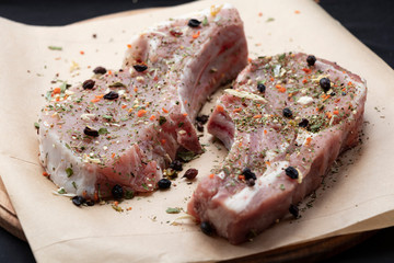 Pink raw pork steaks lie on a wooden board in spices and green dill. Appetizing meat. On kraft paper and a black background.