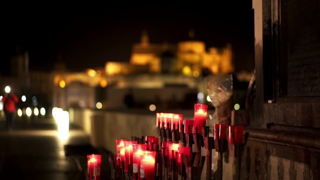 Pan shot left to right of Saint Raphael statue at night on the Roman Bridge of Cordoba. View of Mosque-cathedral, Catedral de Cordoba behind an angel statue on the roman bridge