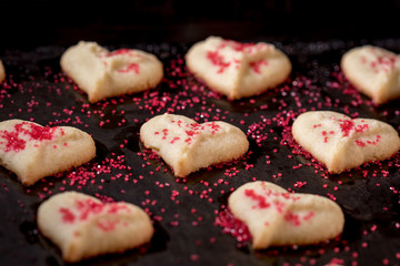 Heart shaped butter spritz cookies on baking sheet with red sugar sprinkles selective focus