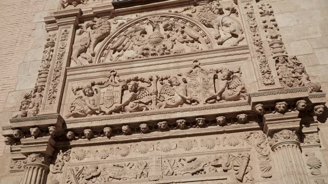 Pan shot left to right of facade of Archaeological Museum of Granada, with figures on wall. Details of the facade upon the door of Granada Museum