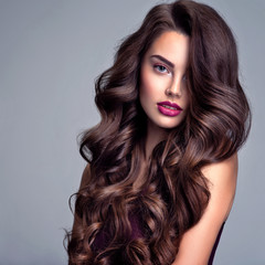 Face of a beautiful woman with long brown curly hair. Fashion model with wavy hairstyle. Attractive...